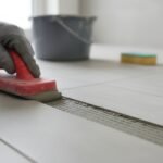 Applying grout between ceramic floor tiles using a rubber grout float during tile installation
