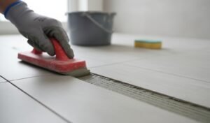 Applying grout between ceramic floor tiles using a rubber grout float during tile installation