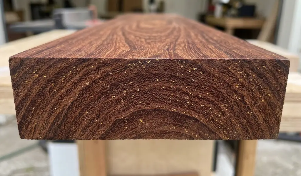 Detailed macro photo of Teak wood surface grain, showcasing its straight, tight golden-honey brown pattern and smooth, oily texture.